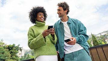Two professionals engage with mobile devices on a modern balcony, symbolizing seamless digital collaboration and intelligent connectivity.